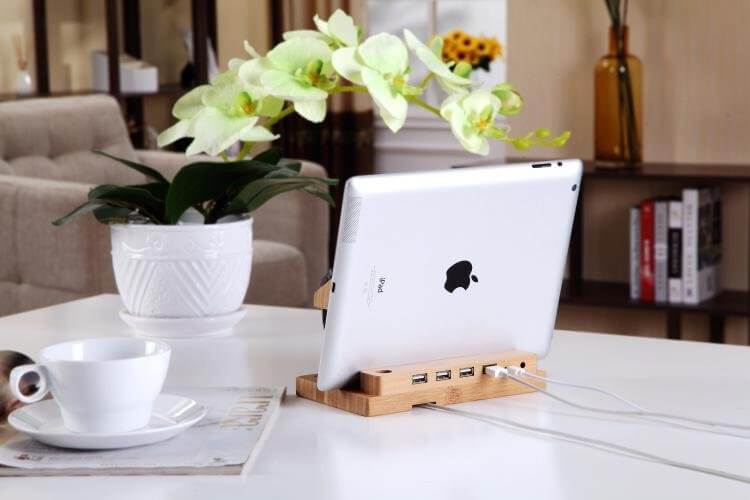 Bamboo docking station with 4 USB ports holding an iPad, set in a stylish home environment with plants and coffee.