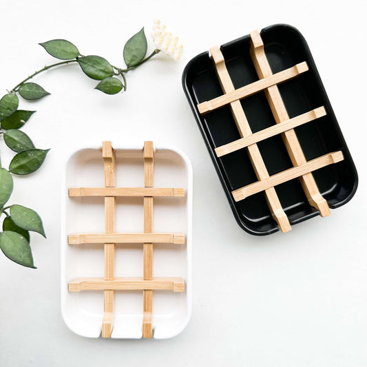 Biodegradable bamboo and cornstarch soap dishes in black and white with removable bamboo grid for soap drainage.