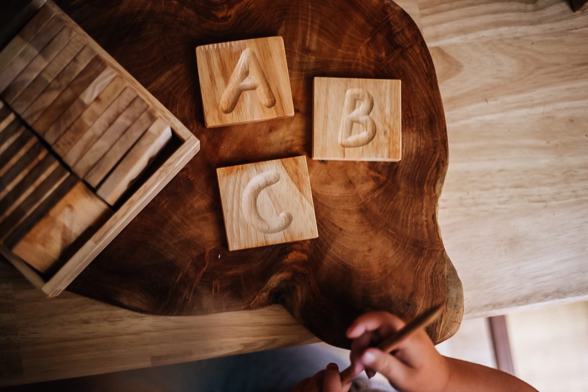 Montessori-style wooden capital letter tiles A, B, C on a natural wood tray, promoting early literacy skills.