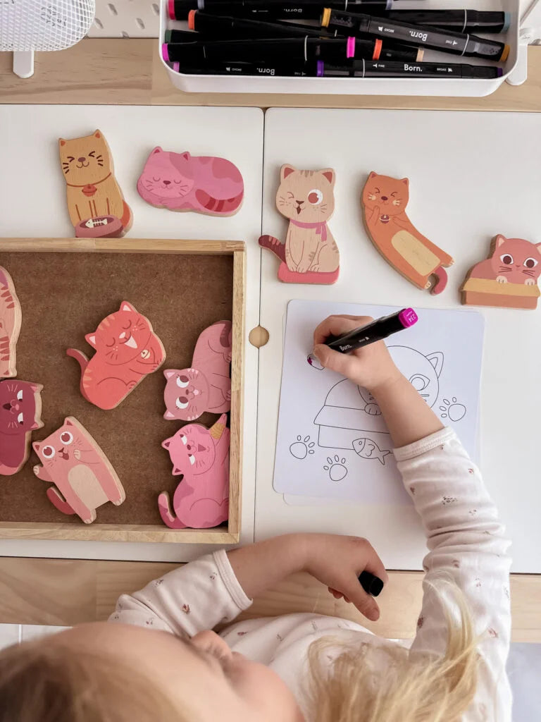 Child coloring with a marker while playing with wooden cat toys in a creative activity set.
