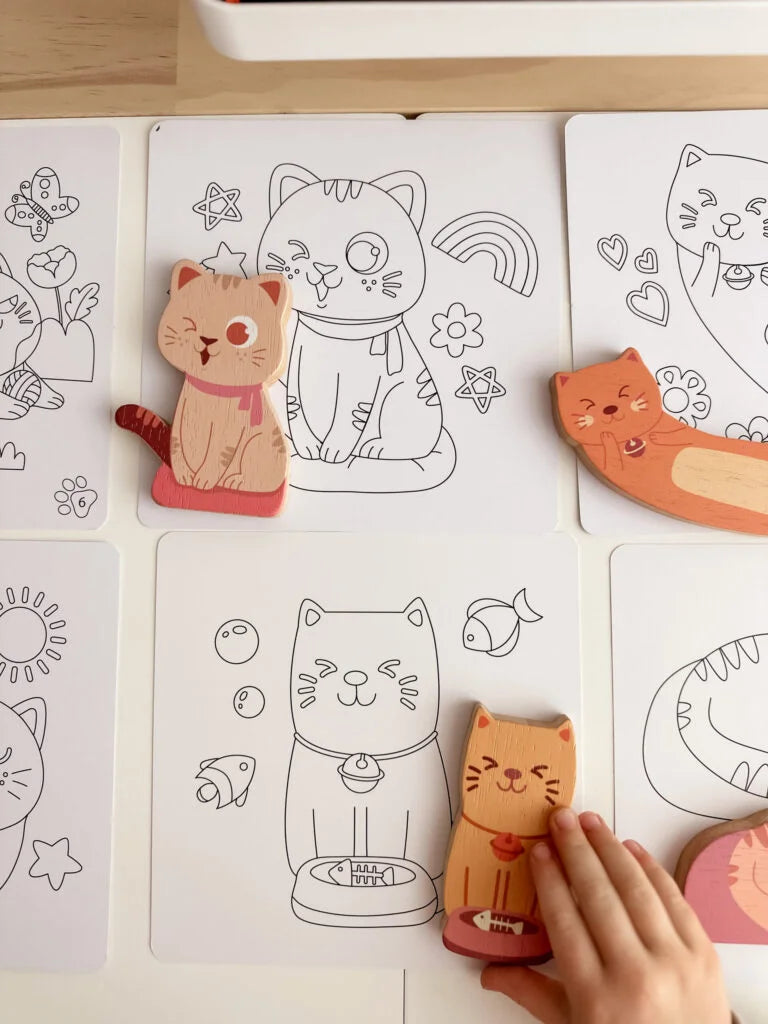 Child hands playing with wooden cat figures on coloring cards, fostering creativity and imagination.