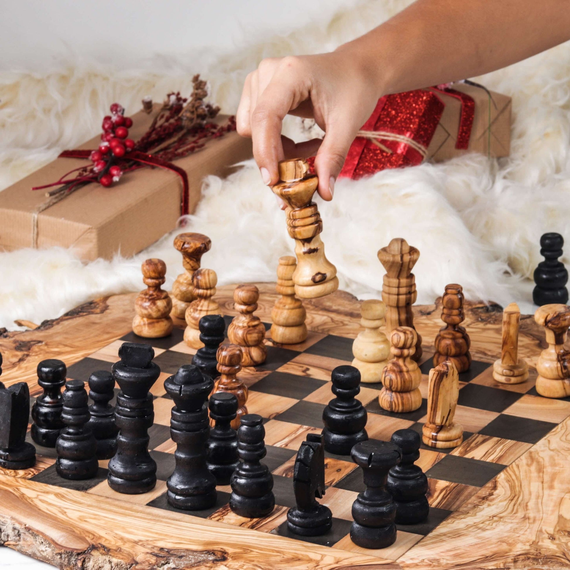 Handcrafted olive wood chess set in play with unique grain patterns on rustic board, surrounded by holiday decor.