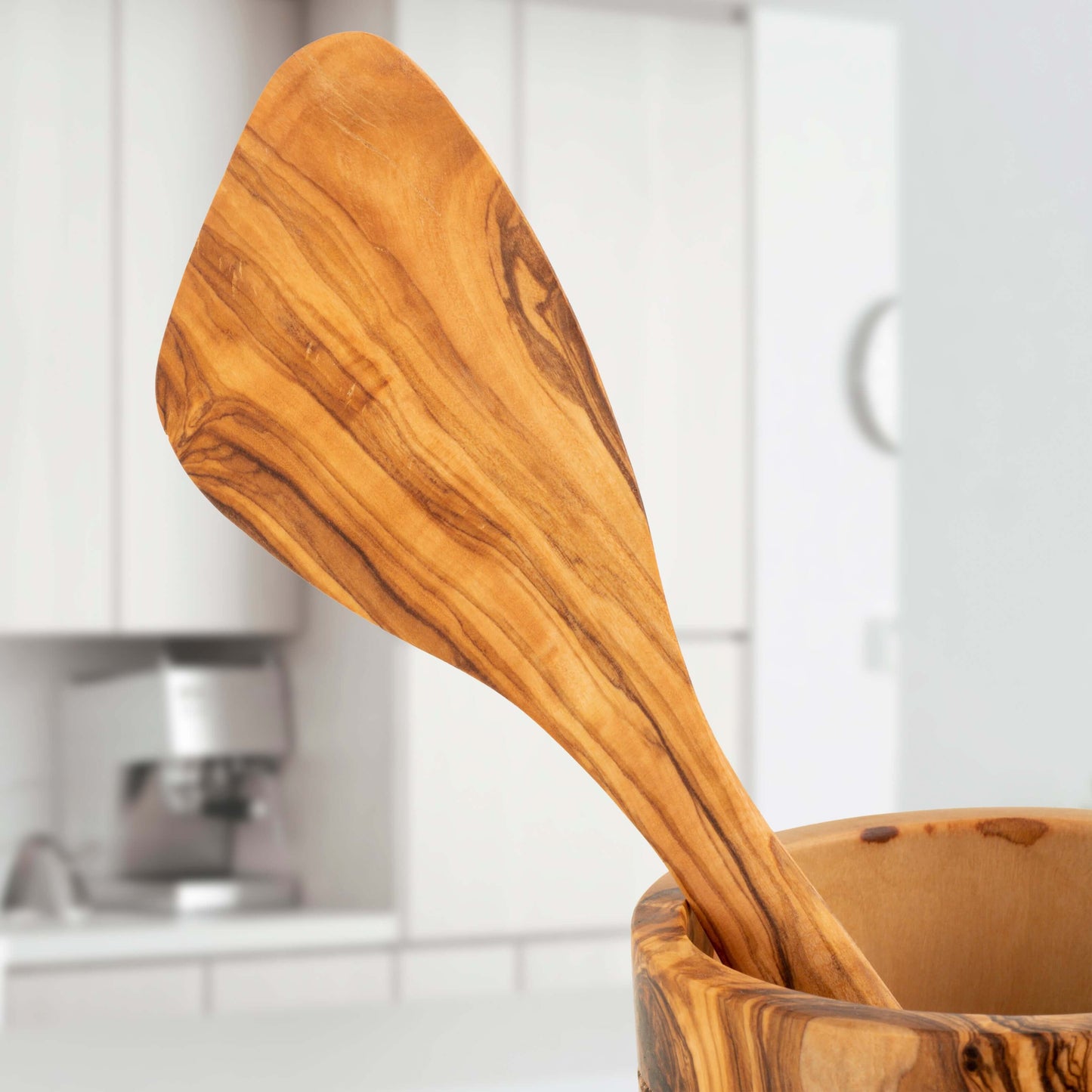 Handmade olive wood spatula with unique grain pattern, showcased in a modern kitchen setting.