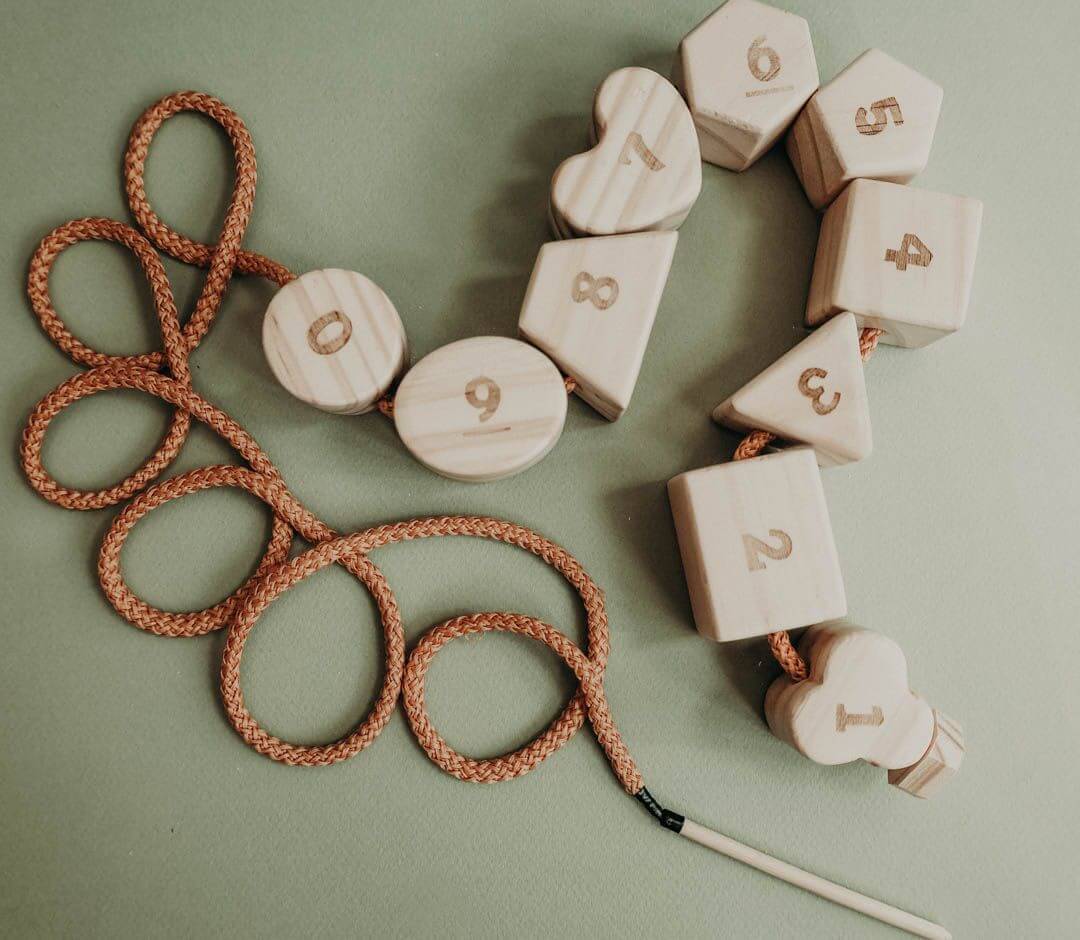 Wooden lacing toy featuring numbers and geometric shapes, promoting fine motor skills and hand-eye coordination.