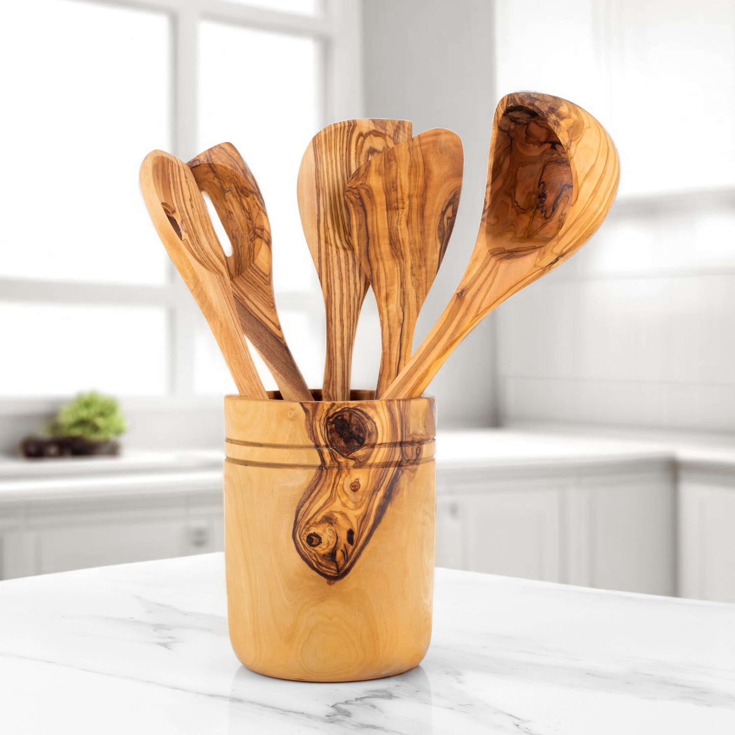 Handmade olive wood kitchen utensils set in wooden holder on a marble countertop, showcasing durable craftsmanship.