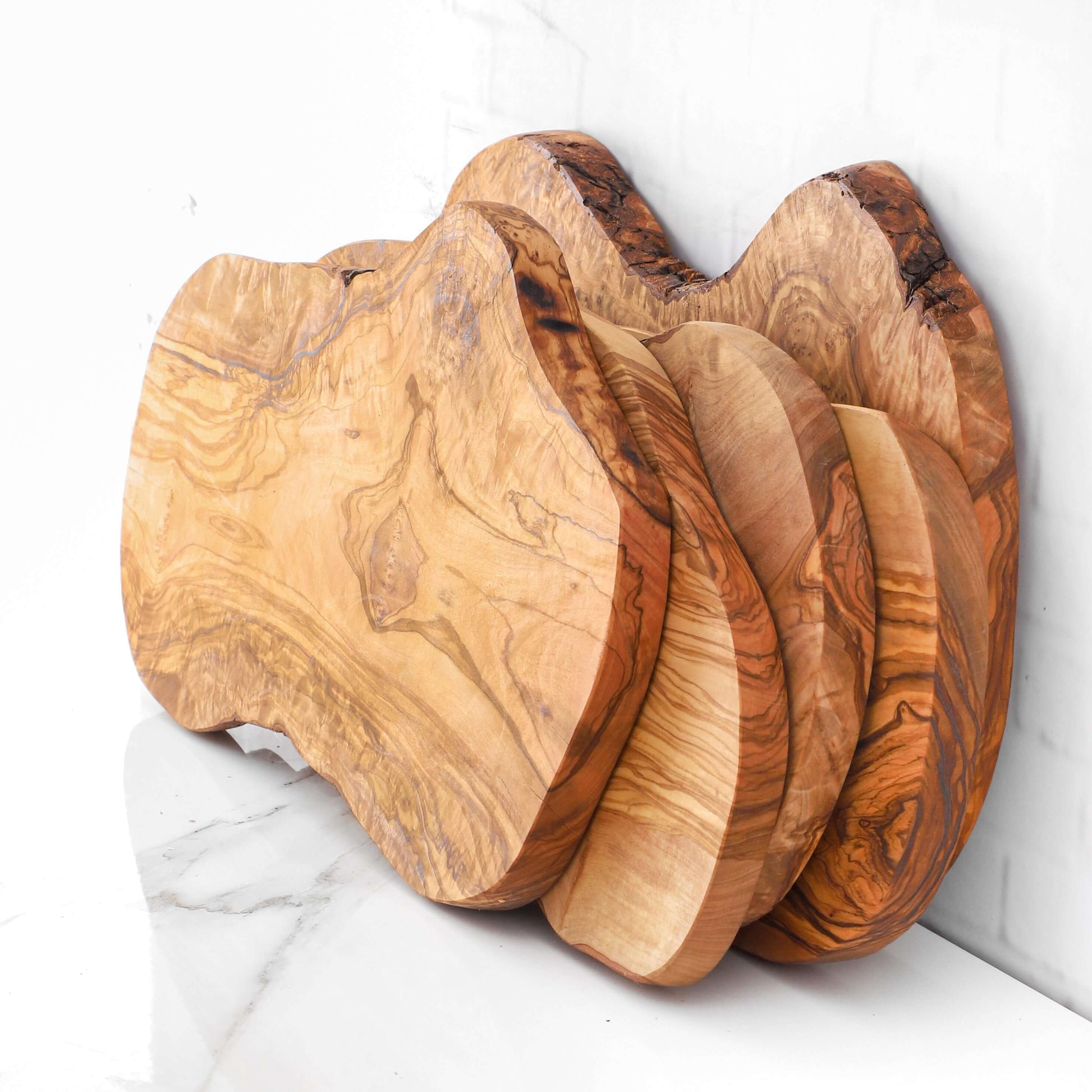Handmade rustic olive wood cutting boards stacked, showcasing unique natural edges and durable surfaces.