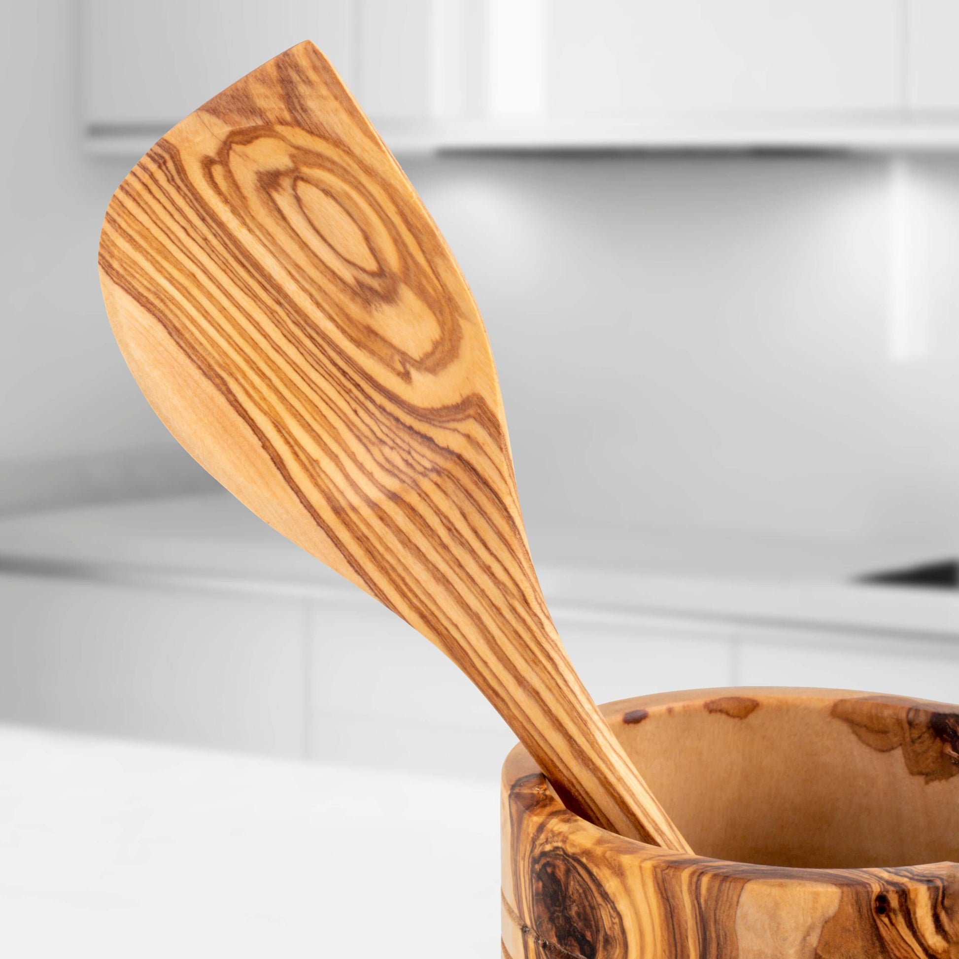 Handmade olive wood spatula resting in a wooden holder, showcasing unique grain patterns and craftsmanship.