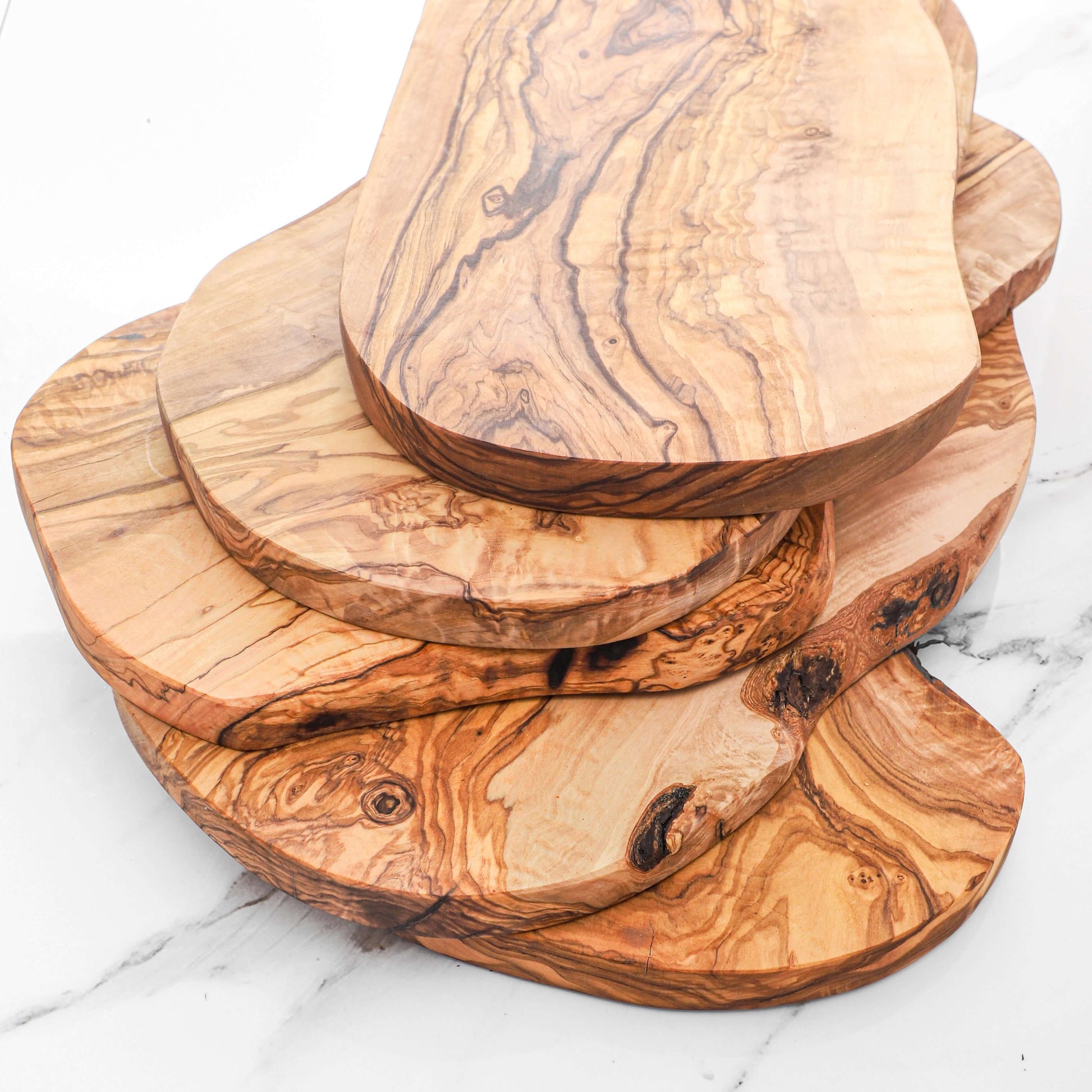 Stack of handmade rustic olive wood cutting boards showcasing unique natural edges and rich grain patterns.