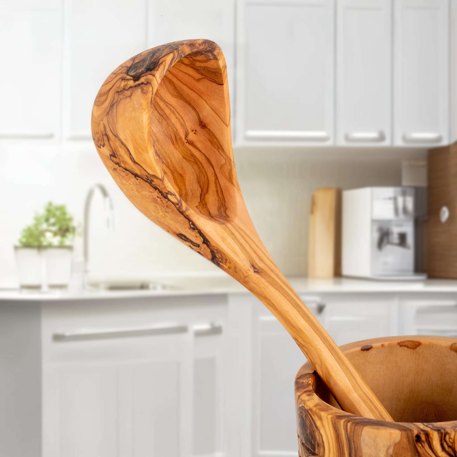 Handcrafted olive wood ladle in a kitchen setting, showcasing beautiful grain and durability.