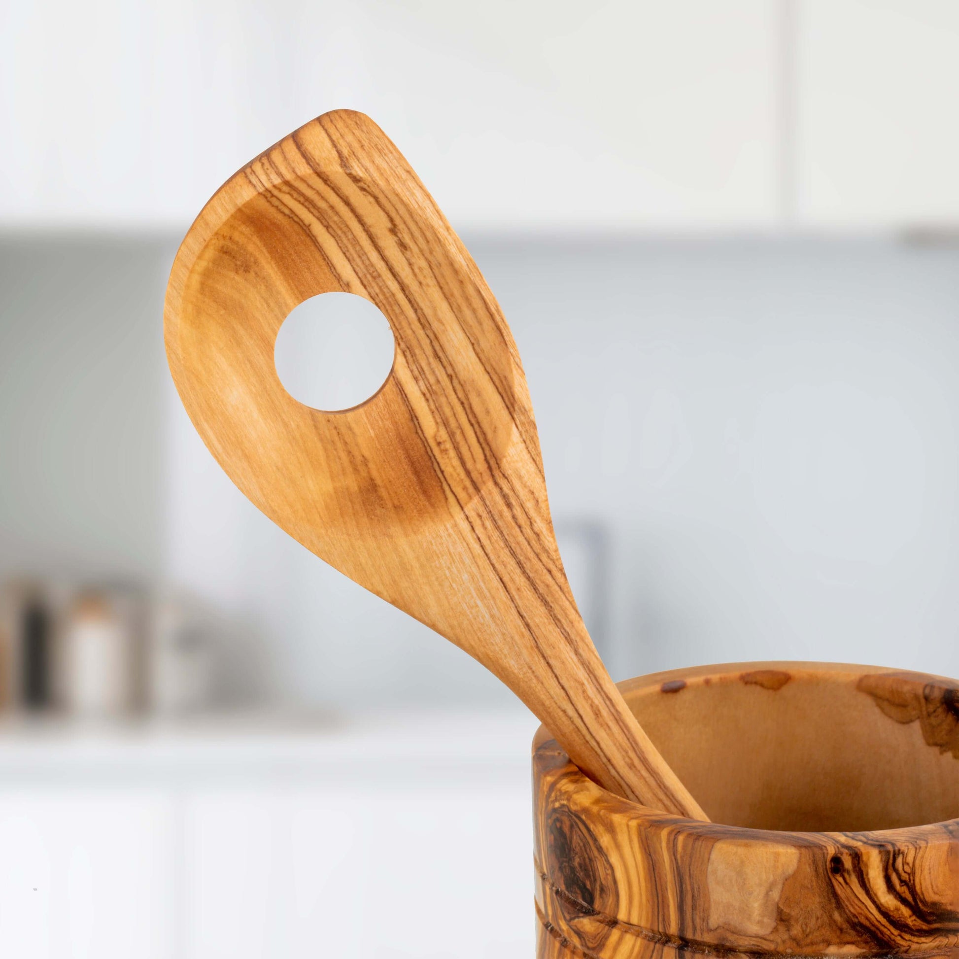 Handmade olive wood ladle resting in a polished wooden holder, showcasing its durable craftsmanship and unique design.