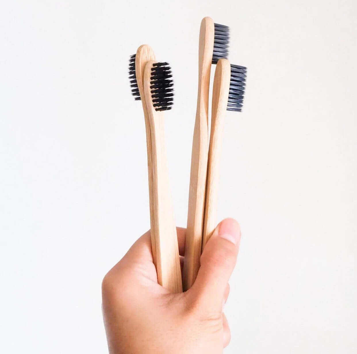 Eco-friendly bamboo toothbrushes with activated charcoal bristles held in hand for sustainable oral care.