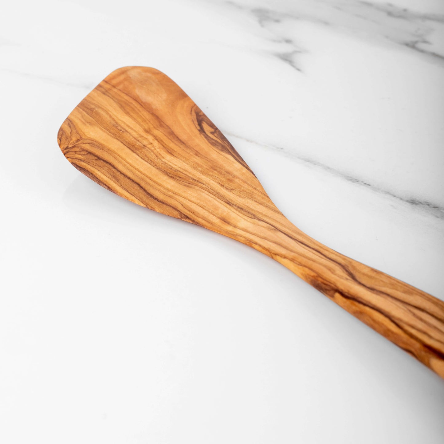 Handmade olive wood corner spatula with a unique flat edge for precise cooking on a marble surface.