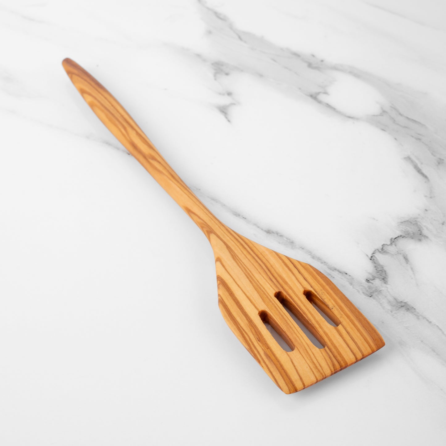 Handmade olive wood slotted spatula on a marble surface, perfect for flipping and stirring in the kitchen.
