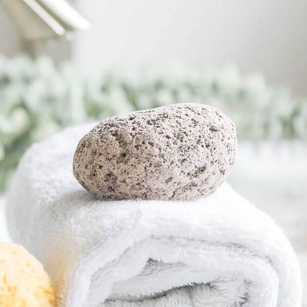 Natural lava stone pumice foot scrubber resting on a white towel, promoting zero waste skin care.