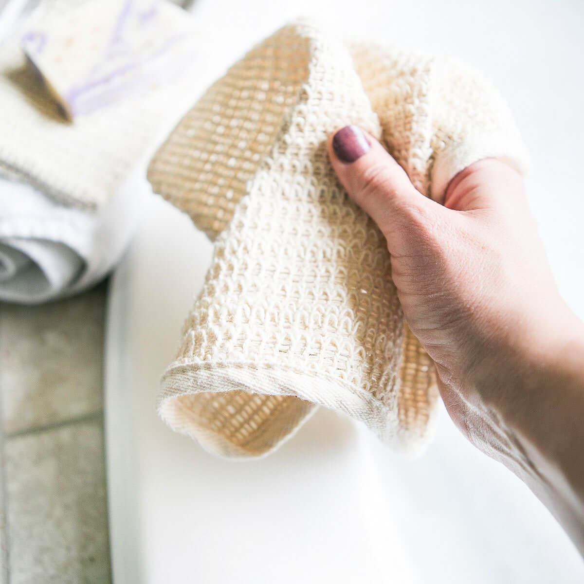 Hand holding a natural sisal washcloth for gentle exfoliation, showcasing its organic and plastic-free design.