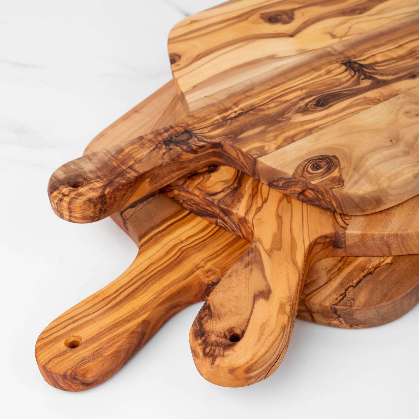 Stacked olive wood cutting boards with handles showcasing unique grain patterns and artisanal craftsmanship.