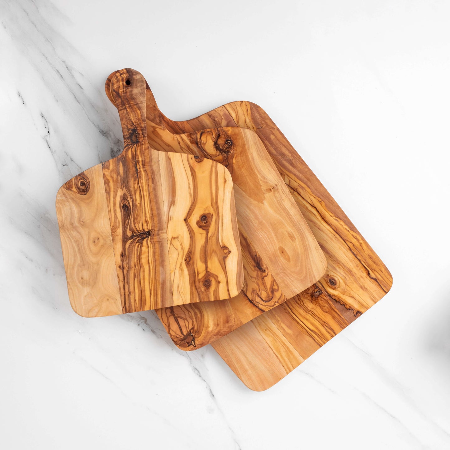Set of three handmade olive wood cutting boards with handles, showcasing unique grain patterns for durability and style.