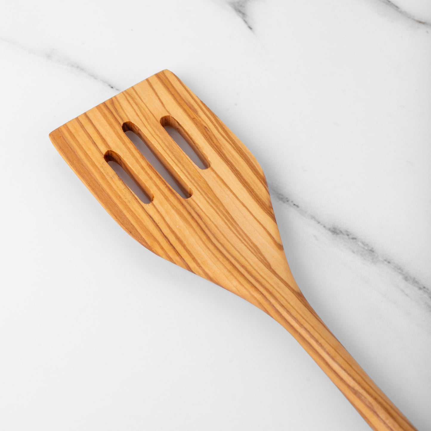 Handmade olive wood slotted spatula on marble countertop, ideal for cooking and flipping.