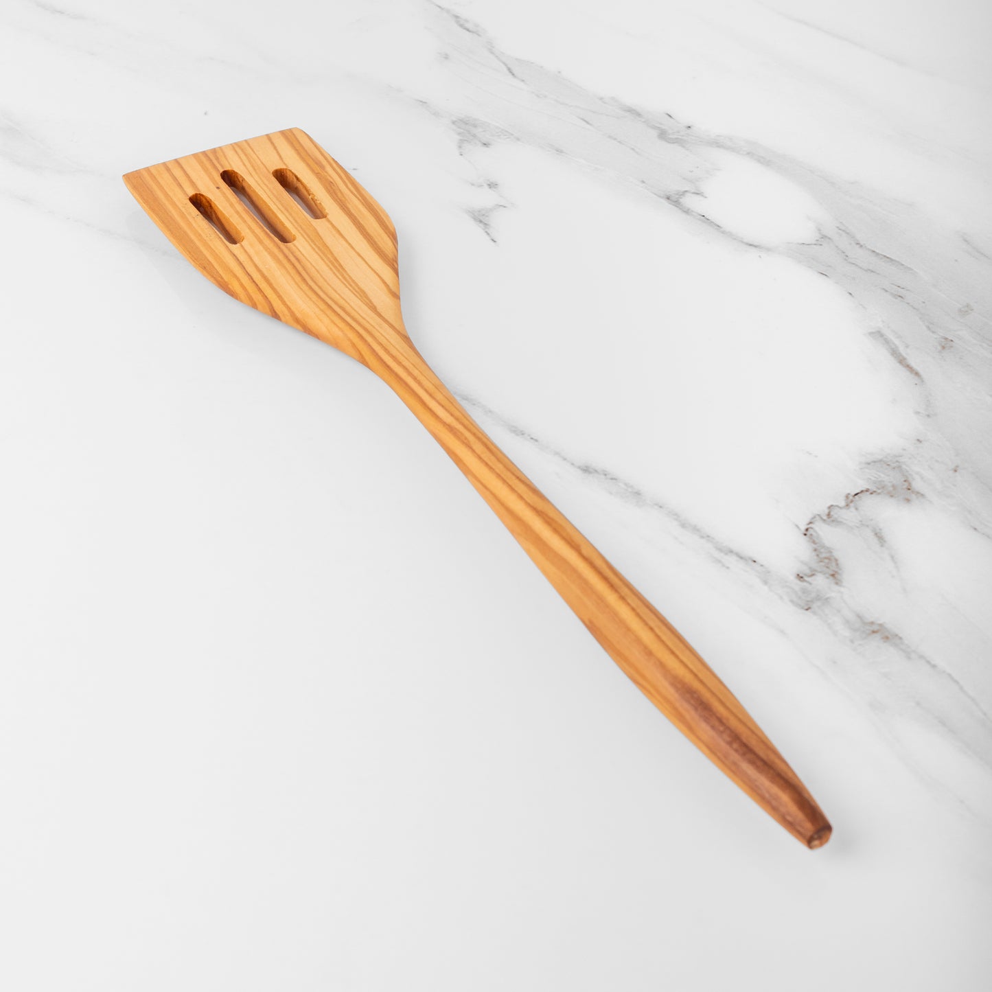 Handmade olive wood slotted spatula on a marble surface, perfect for flipping and stirring in the kitchen.