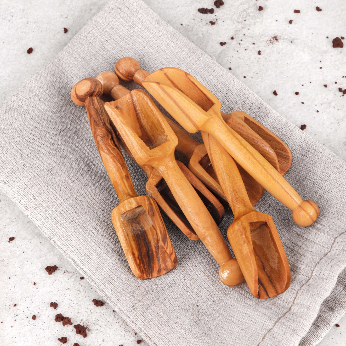 Handcrafted mini wooden scoops made from olive wood, perfect for measuring coffee, sugar, and spices, set on a linen cloth.
