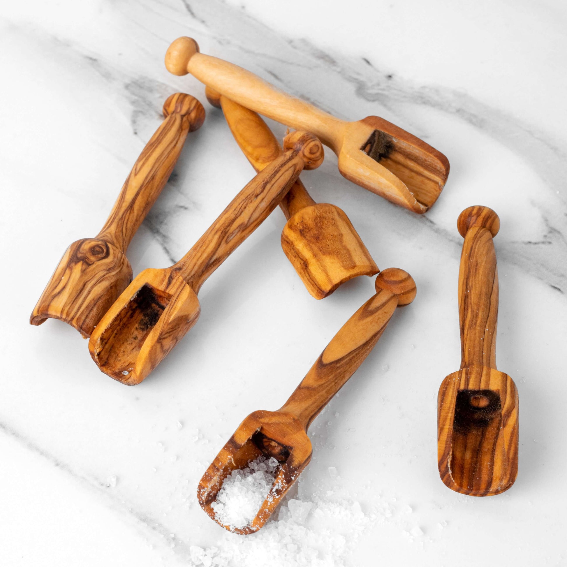 Set of handcrafted mini wooden scoops made from olive wood, ideal for sugar, coffee, and spices on a marble surface.