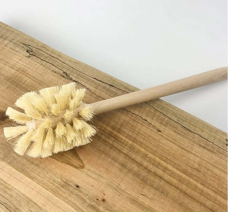 Eco-friendly plastic-free toilet brush with natural sisal bristles on wooden surface.