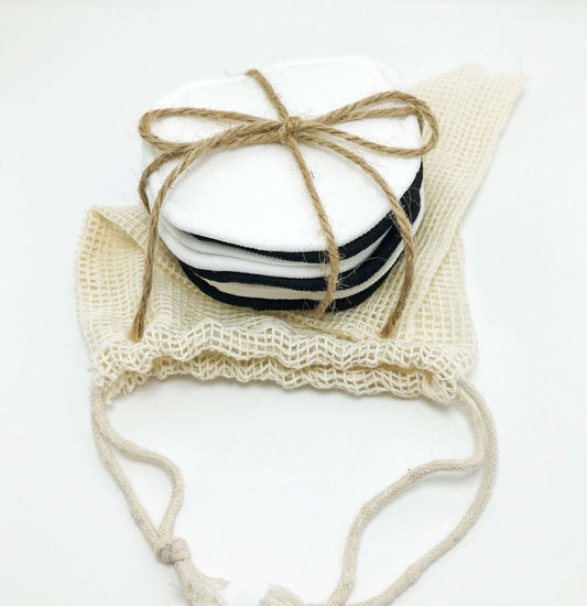 Stack of reusable organic bamboo cotton facial pads tied with twine, included in a natural mesh bag.