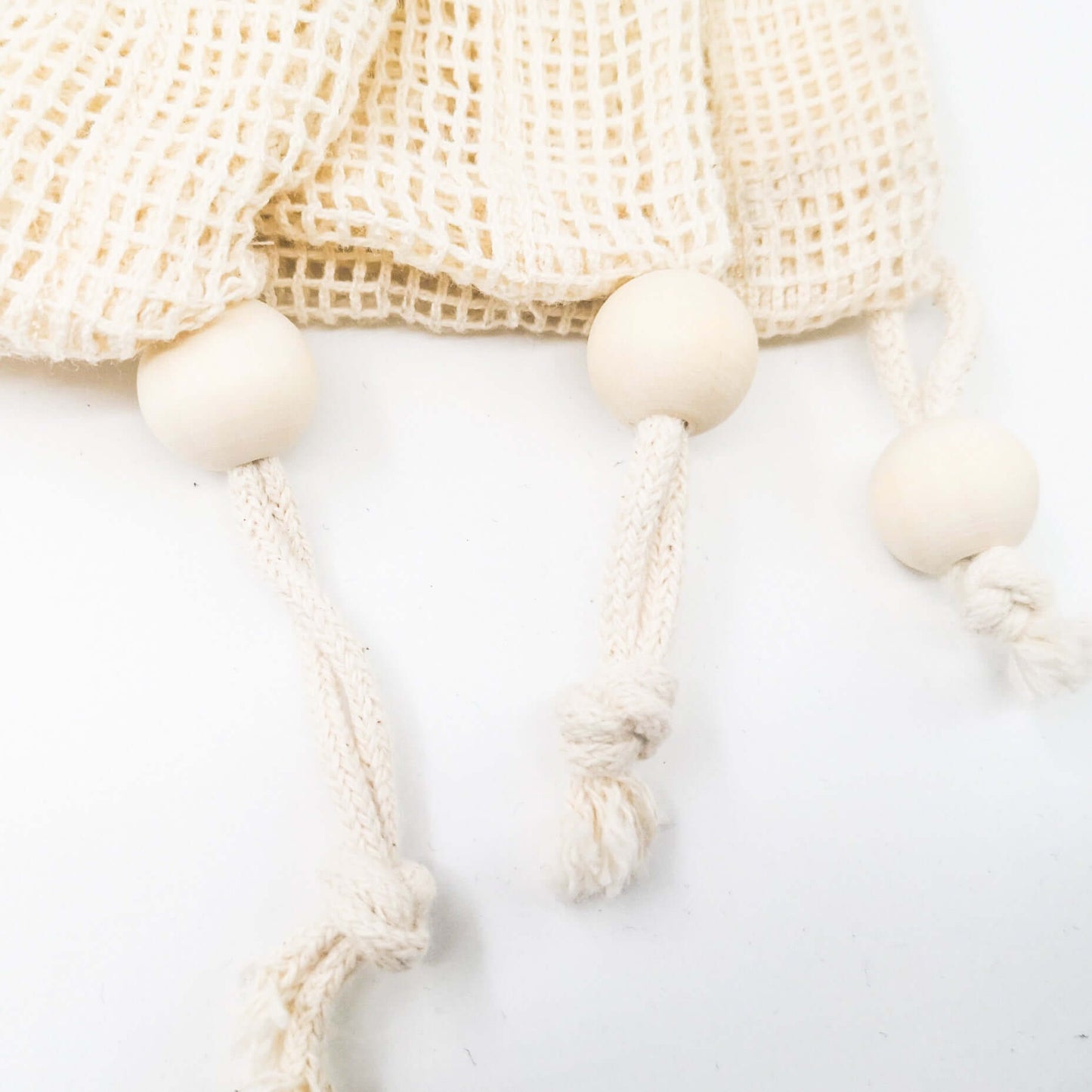 Close-up of reusable organic cotton mesh produce bag with wooden drawstring beads for zero waste shopping.