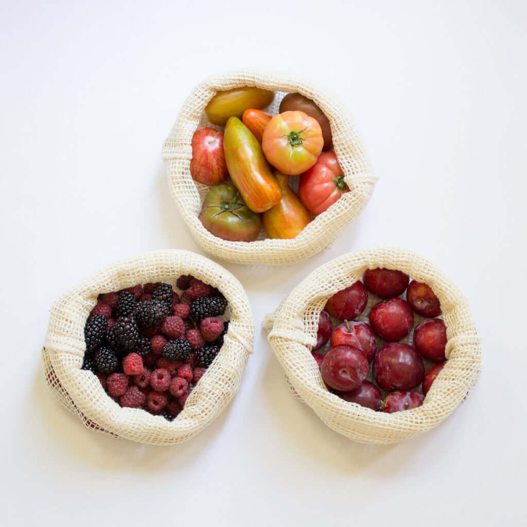 Three reusable organic cotton mesh bags filled with fresh fruits and vegetables, promoting a zero waste lifestyle.