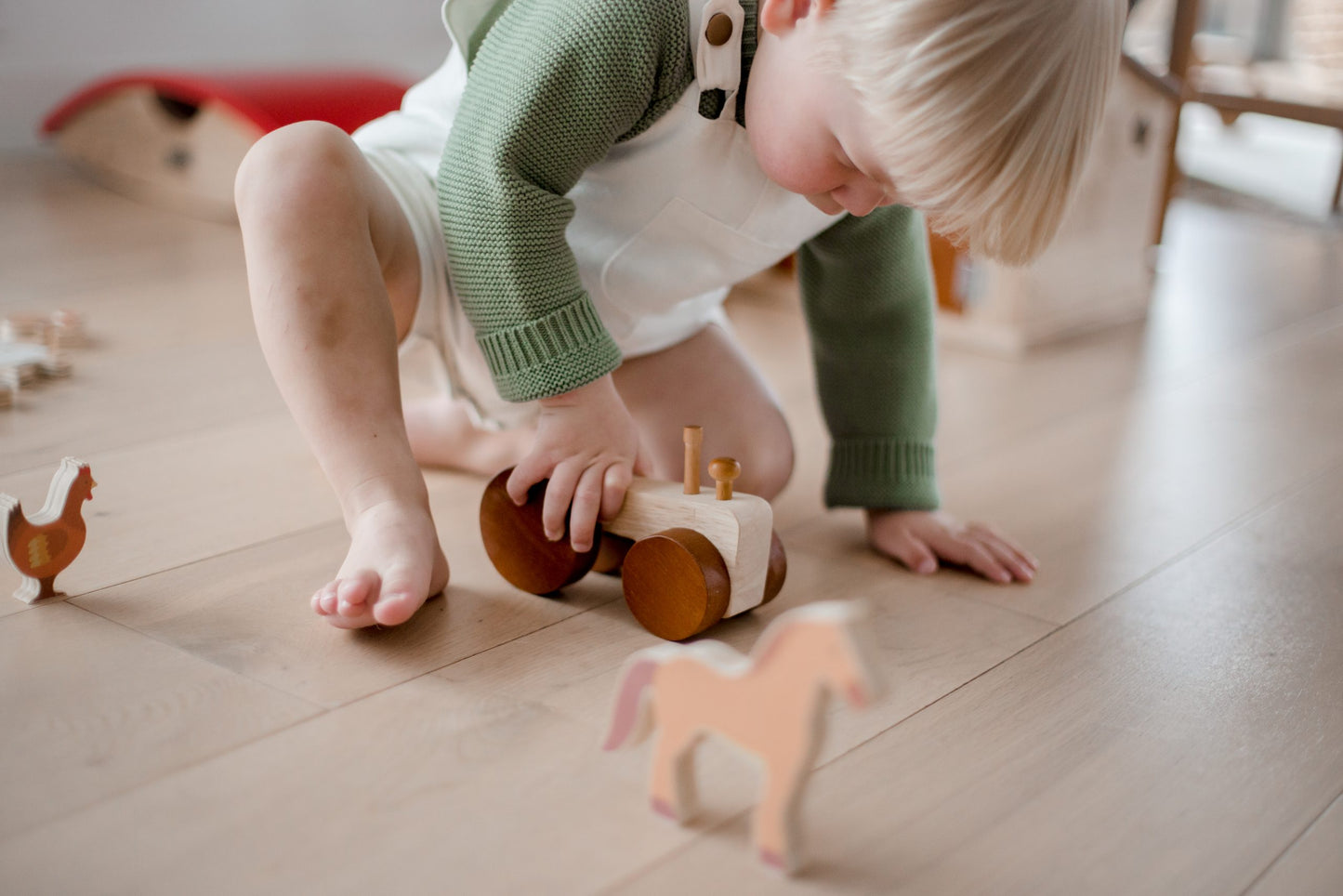 Toddler playing with a wooden tractor and farm animal figures on the floor to promote imaginative play.