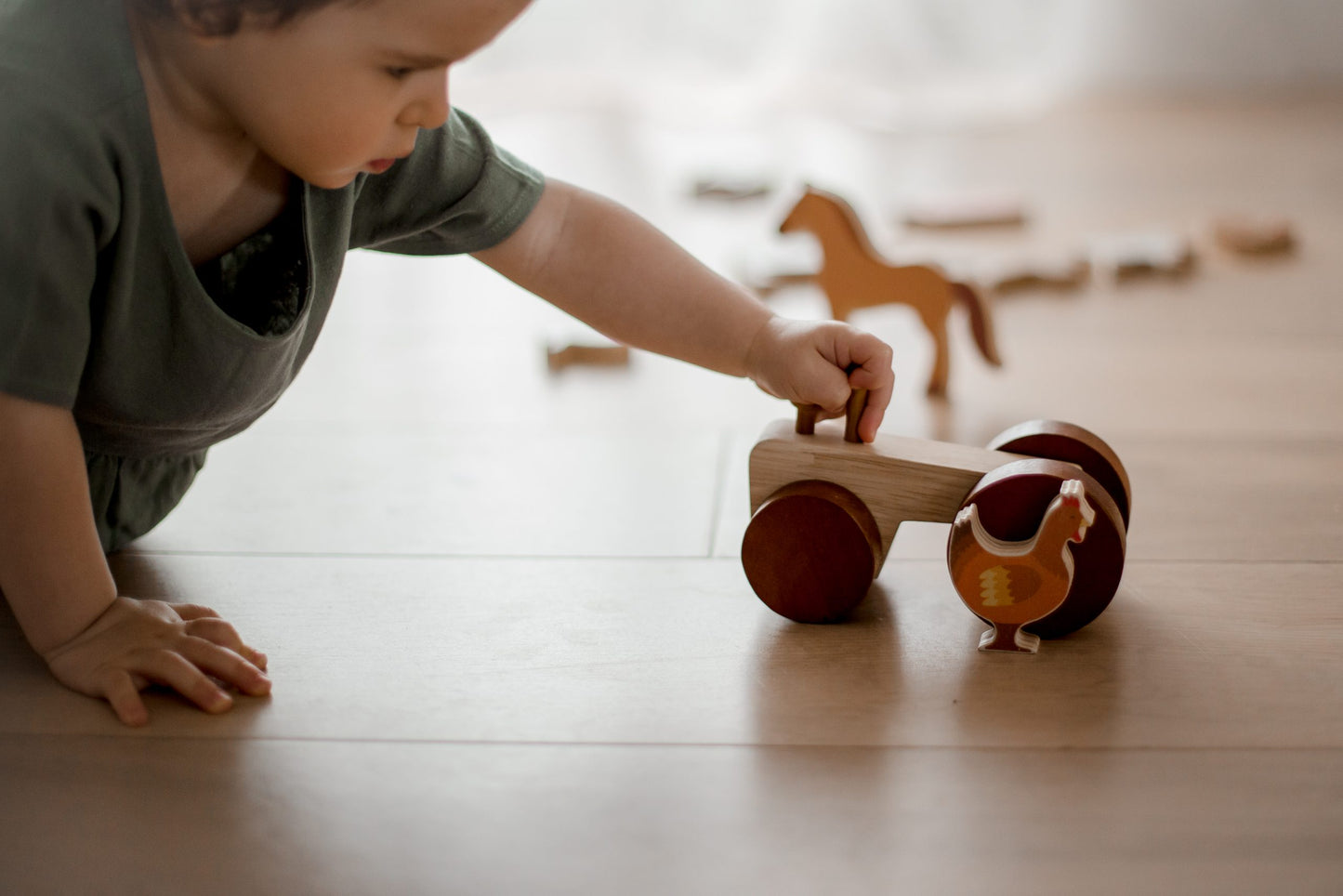 Toddler playing with wooden tractor and animal figurine on the floor, promoting imaginative pretend play.