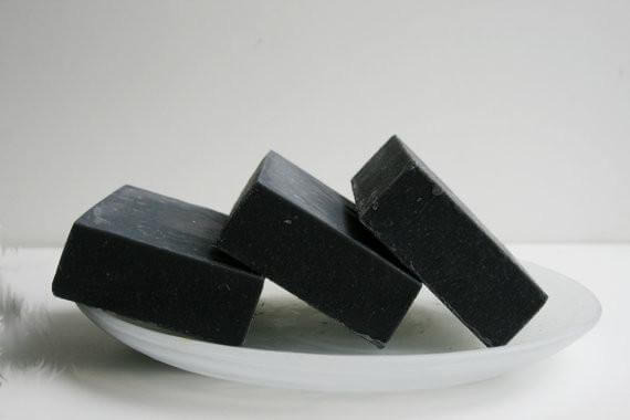 Three bars of unscented activated charcoal soap stacked on a white plate, ideal for sensitive skin and pore cleansing.