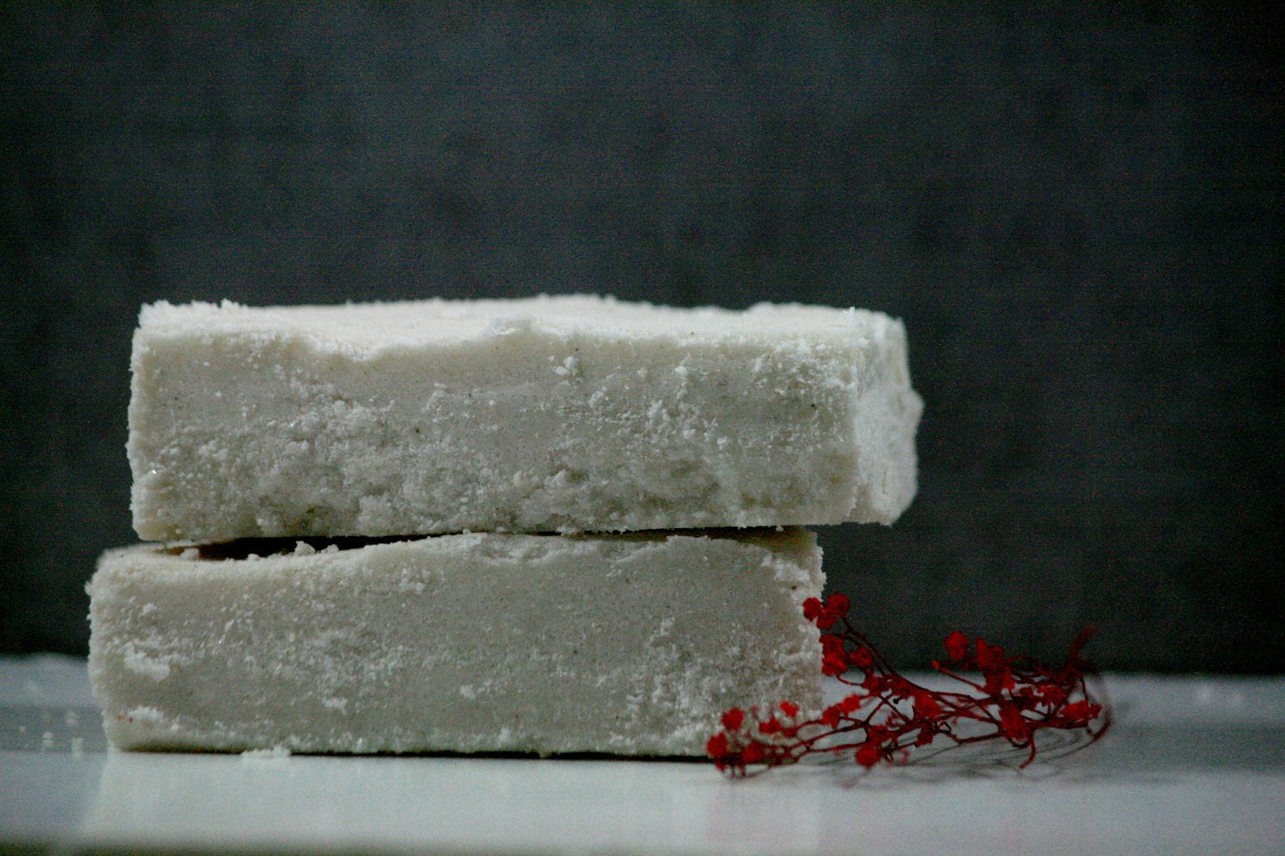 Two stacked white sea salt bars with a red flower on a surface, showcasing a soothing skincare product.