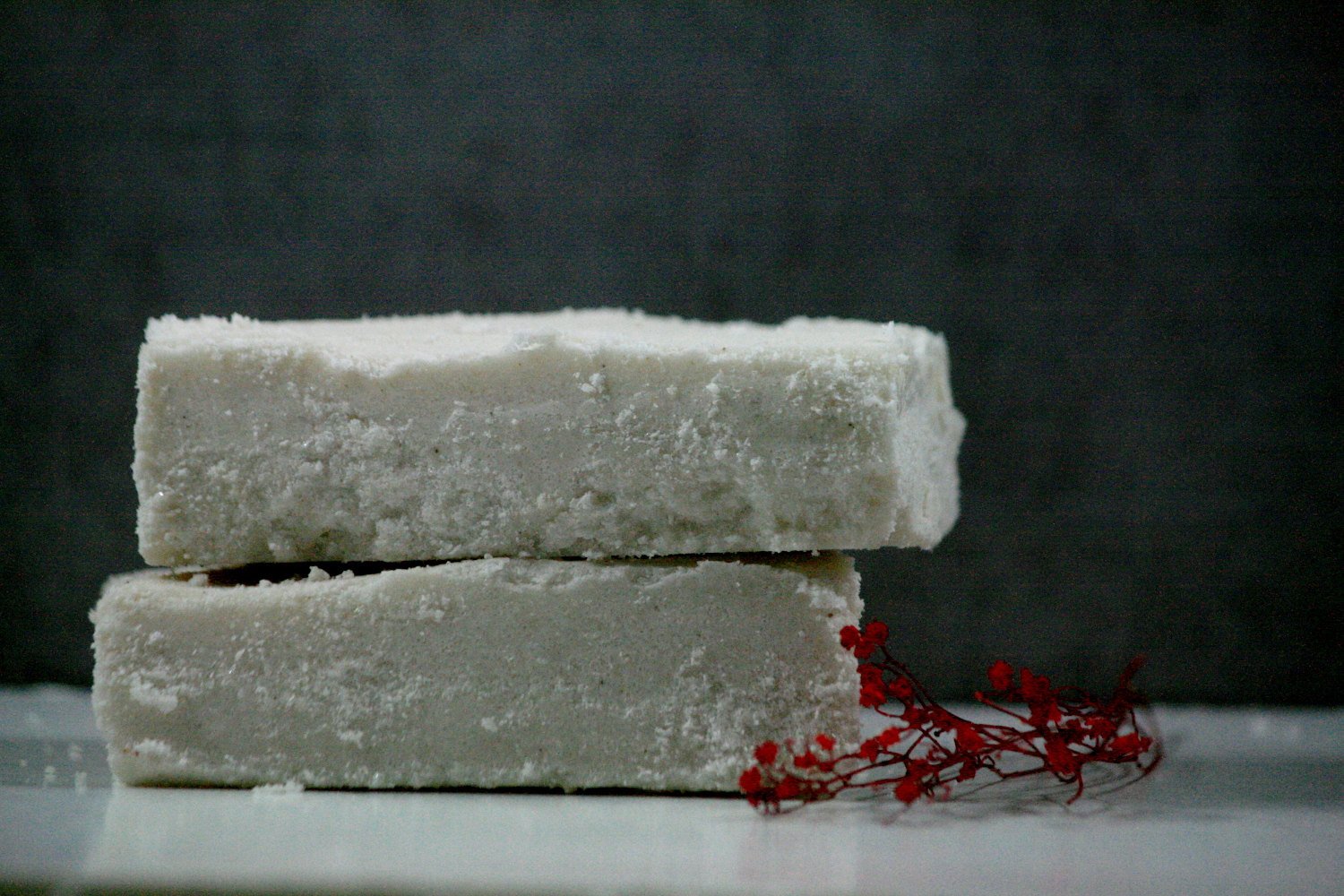 Two stacked white sea salt bars with a red flower on a surface, showcasing a soothing skincare product.