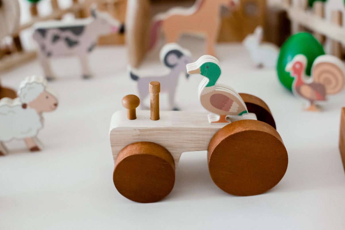 Wooden tractor toy with a duck figure, part of a colorful farm animal play set for toddlers.