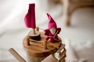 Wooden windmill toy with vibrant red flags and a whimsical figure, promoting imaginative play and creativity for toddlers.
