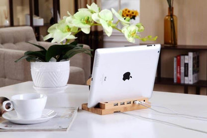 Bamboo docking station with 4 USB ports holding an iPad, set in a stylish home environment with plants and coffee.