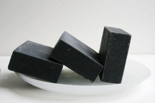 Three pieces of handmade activated charcoal soap on a white plate, featuring natural cleansing properties.