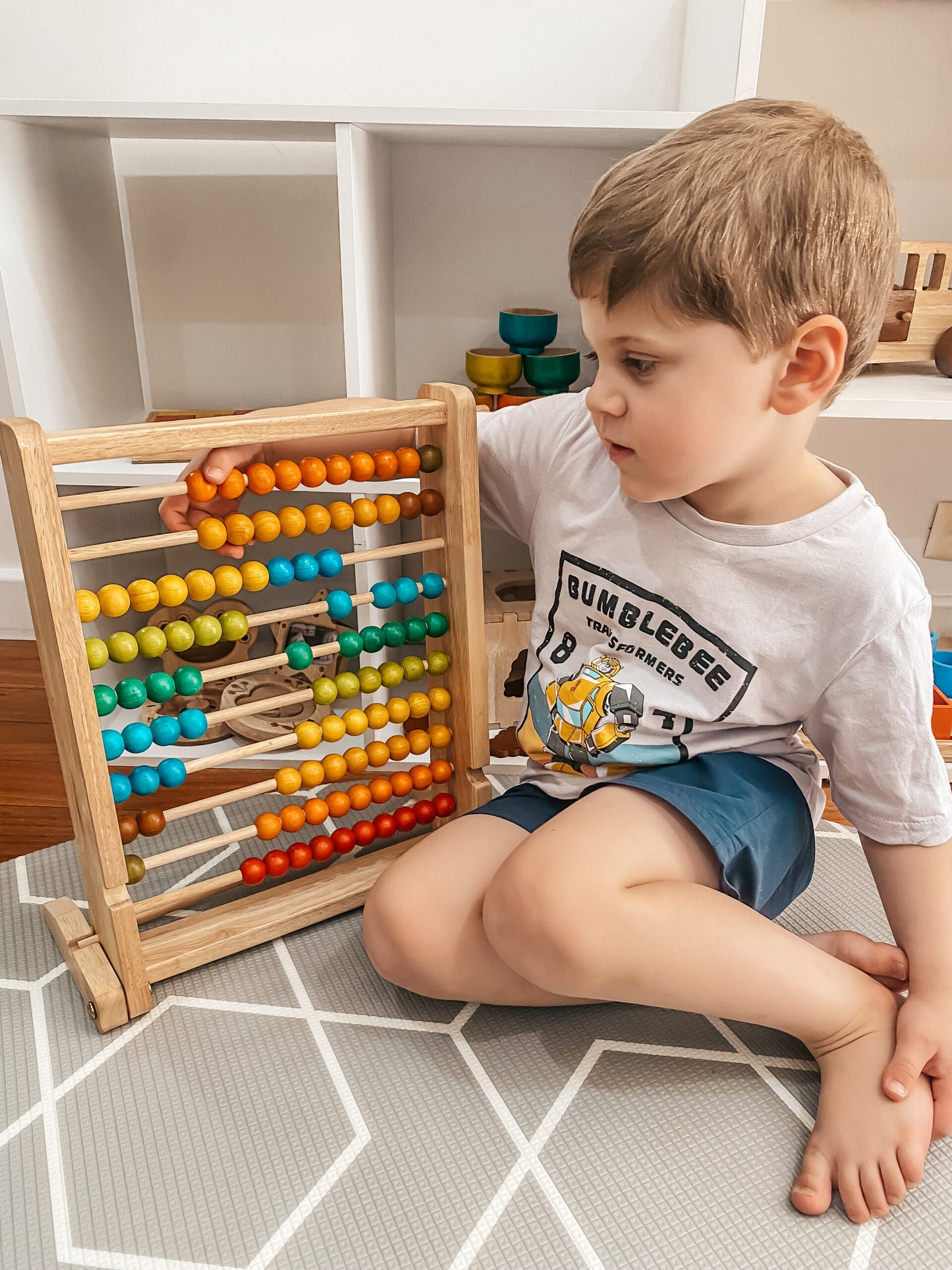 Child engaging with colorful wooden bead counting abacus, learning math skills through play.