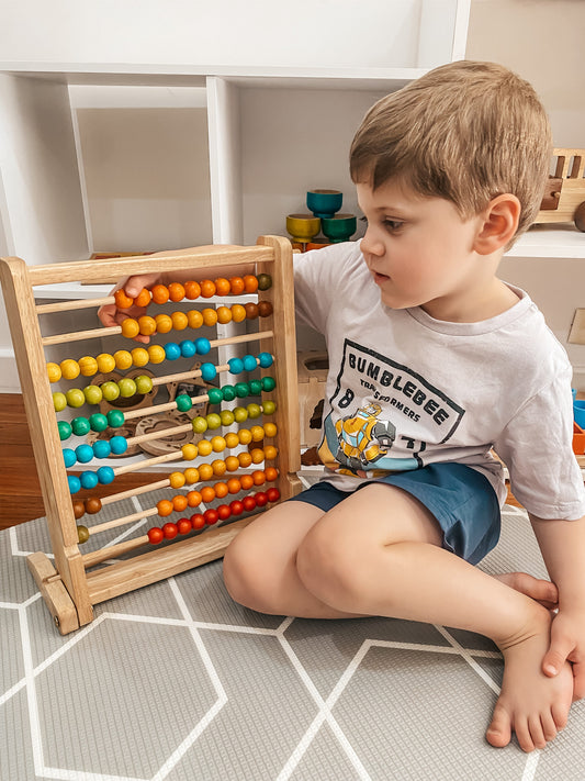 Child engaging with colorful wooden bead counting abacus, learning math skills through play.