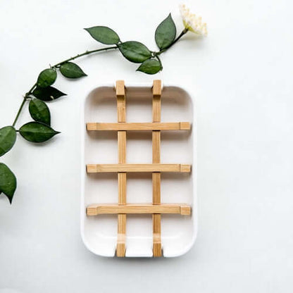 Biodegradable bamboo and cornstarch soap dish with removable grid for drainage against a light background.