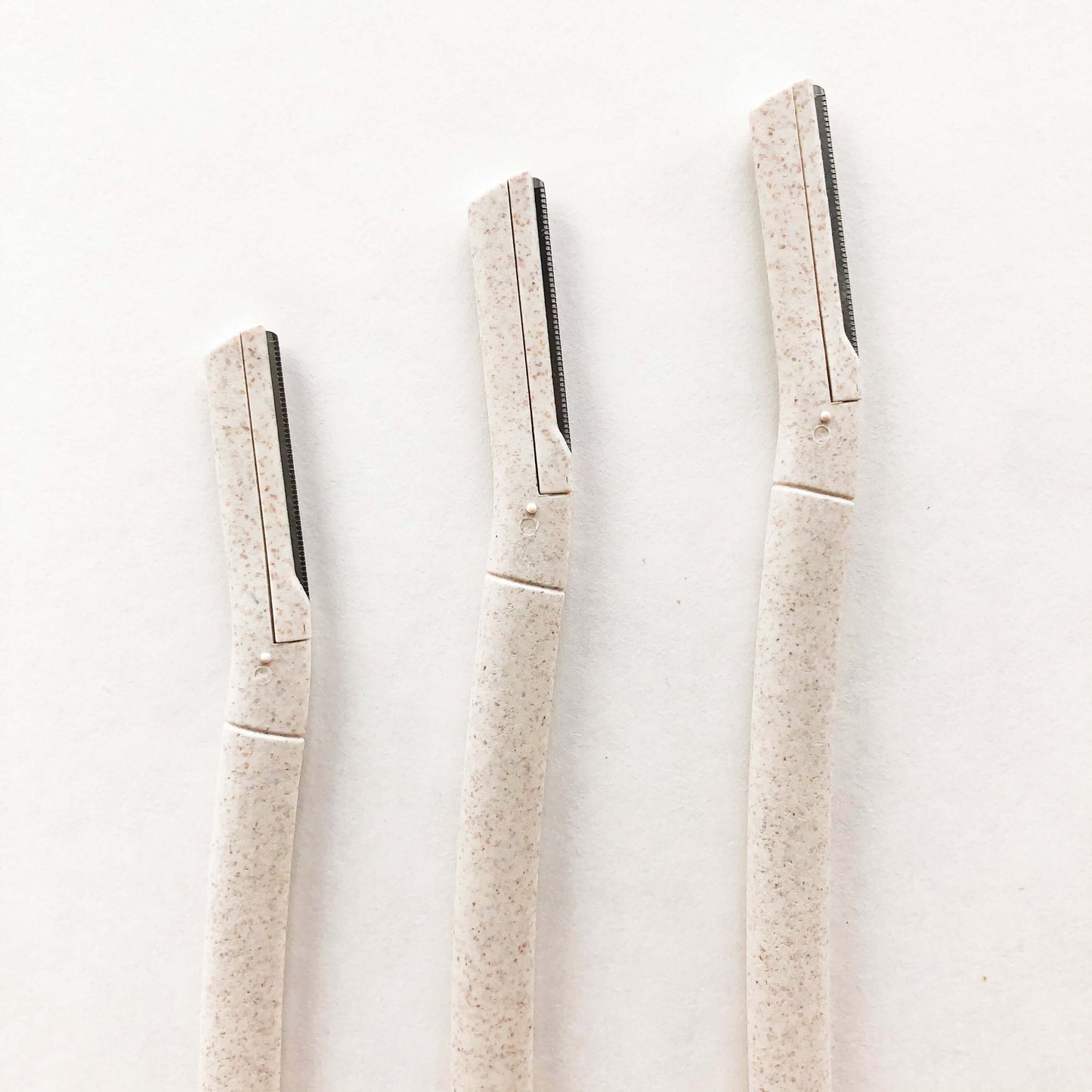 Three biodegradable wheat straw eyebrow razors lined up on a plain background, eco-friendly beauty tools for flawless brows.