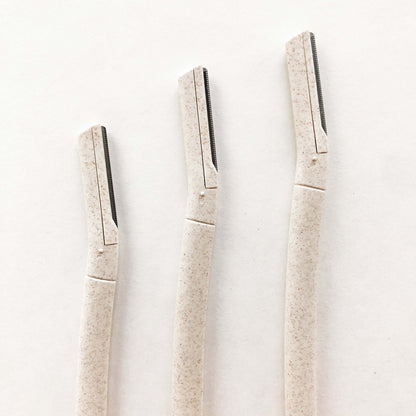 Three biodegradable wheat straw eyebrow razors lined up on a plain background, eco-friendly beauty tools for flawless brows.