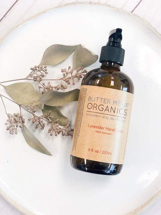 Butter Me Up Organics Lavender Hand Soap bottle on a plate with greenery, natural ingredients for gentle hand care.