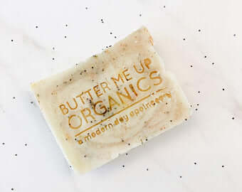 Butter Me Up Organics natural soap bar with exfoliating ingredients on a speckled background.