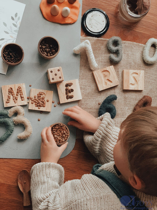 Child engaging with Montessori-inspired alphabet learning tray with wooden letters and sensory materials.