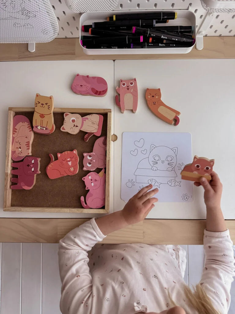 Child playing with wooden cat figures and colouring cards on a table, fostering creativity and imagination.