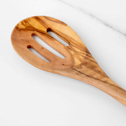 Handmade olive wood slotted spoon with a long handle and three drainage slots on a white marble surface.