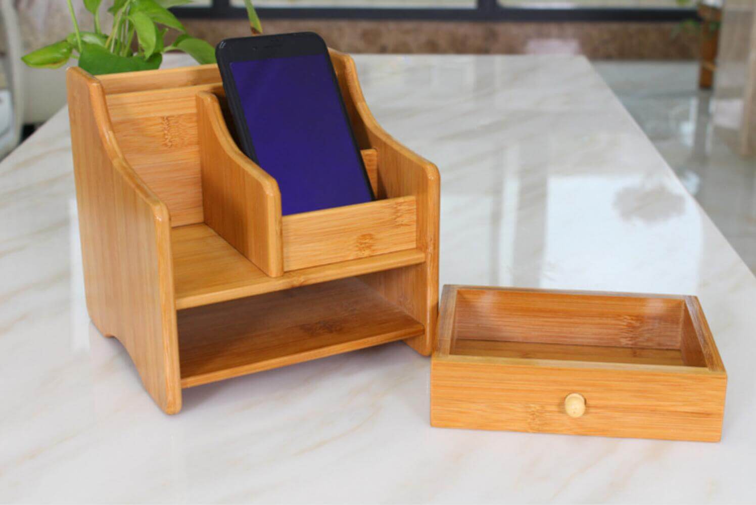 Eco-friendly bamboo storage box with compartments for smartphones, remote controls, and small items on a marble surface.