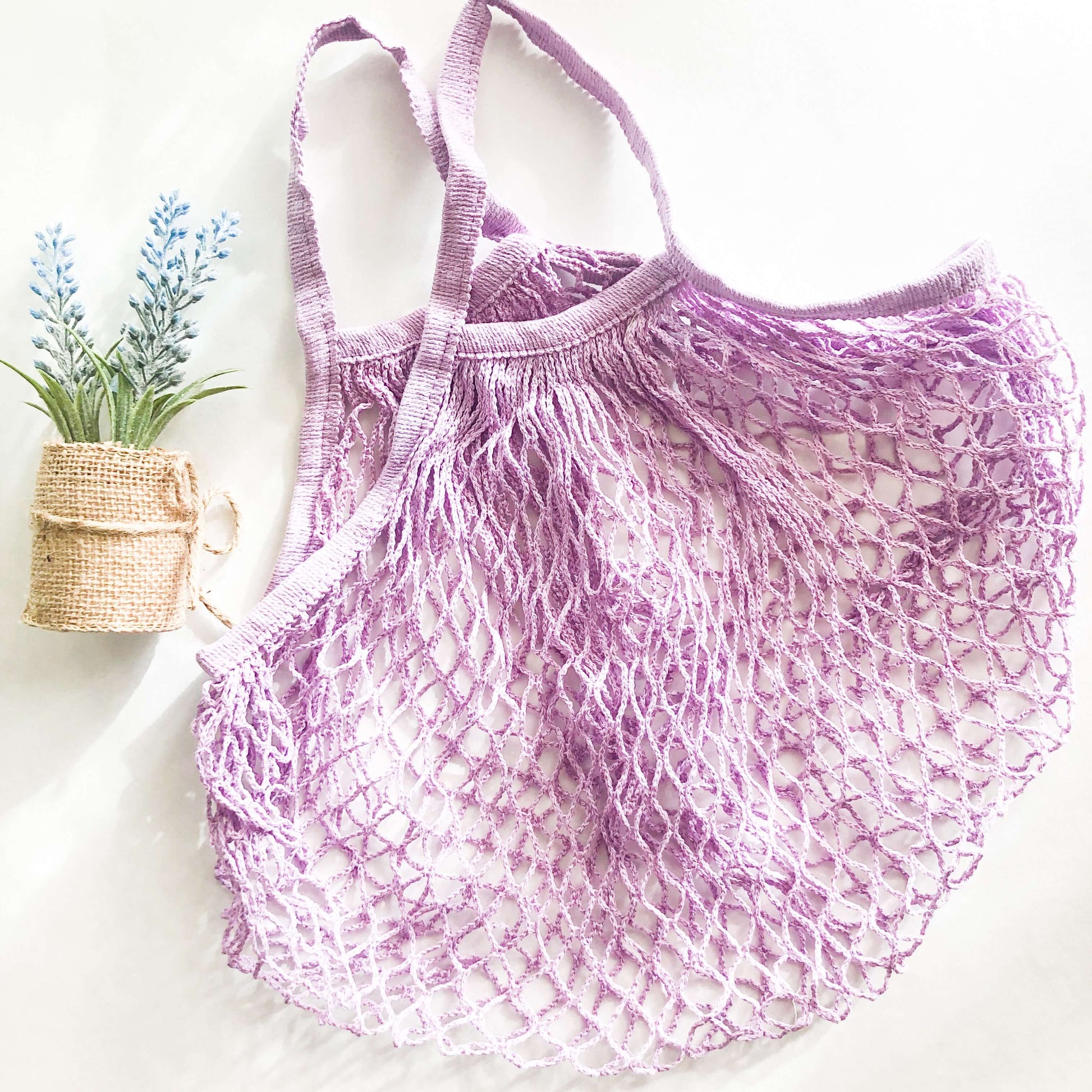 Lightweight purple organic cotton mesh bag next to a small plant, perfect for eco-friendly shopping.